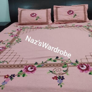 May include: Pink embroidered bedspread and two pillowcases with a floral design. The bedspread features a large embroidered floral border with roses and vines. The pillowcases have a single rose in the center. The text "Naz's Wardrobe" is visible on the bedspread.