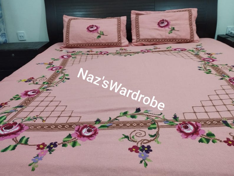 May include: Pink embroidered bedspread and two pillowcases with a floral design. The bedspread features a large embroidered floral border with roses and vines. The pillowcases have a single rose in the center. The text "Naz's Wardrobe" is visible on the bedspread.