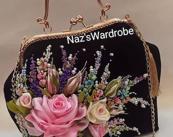 May include: A black velvet handbag with a gold chain strap and a floral design made of ribbons and pearls. The bag has a gold clasp and a gold handle. The text "Naz'sWardrobe" is visible on the bag.