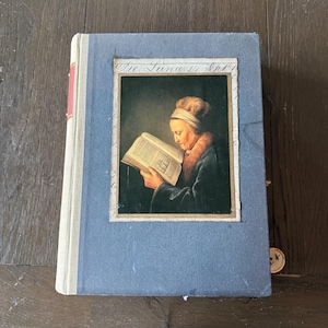 Puede incluir: Un diario vintage con una cubierta azul y un retrato de una mujer leyendo. El retrato está enmarcado y presenta el texto "Die Luna 14 Sept". El lomo del diario es blanquecino con un acento rojo.