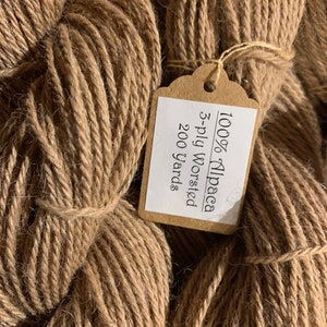 Puede incluir: Una madeja de hilo de alpaca marr&oacute;n con una etiqueta que dice "100% Alpaca 3-ply worsted 200 yards".
