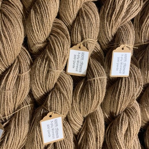 Puede incluir: Primer plano de varios carretes de hilo de alpaca marr&oacute;n con etiquetas de papel que dicen "100% Alpaca 3-ply Worsted 200 Yards".