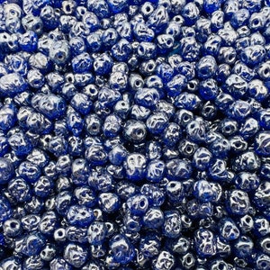 Könnte beinhalten: Nahaufnahme einer großen Menge dunkelblauer Glasperlen. Die Perlen sind facettiert und haben eine glänzende, irisierende Oberfläche.