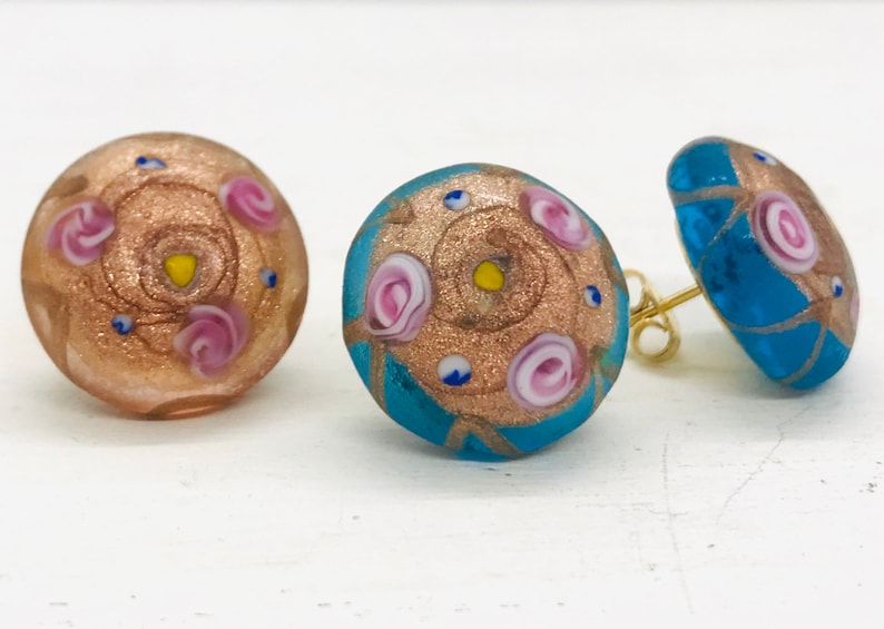 May include: A pair of earrings with a gold and pink floral design on a blue background and a pair of earrings with a gold and pink floral design on a brown background.