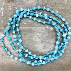 May include: A long necklace made of blue and white striped beads. The necklace is layered and has a circular shape.