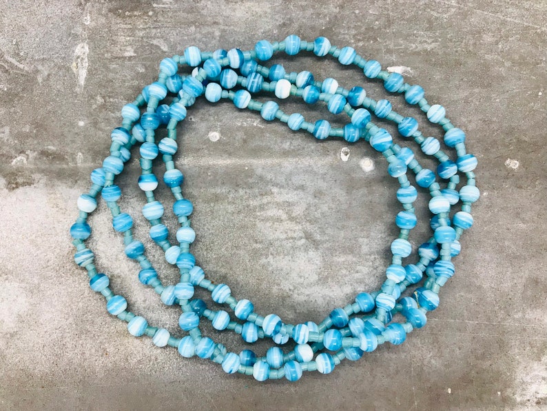 May include: A long necklace made of blue and white striped beads. The necklace is layered and has a circular shape.