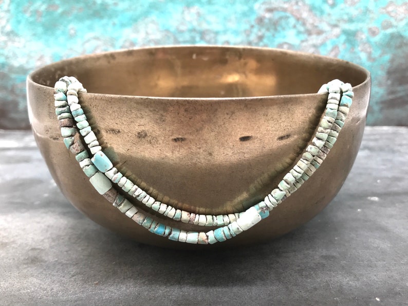 K&ouml;nnte beinhalten: Zwei Str&auml;nge t&uuml;rkisfarbener Perlen in einem hellblauen und wei&szlig;en Farbschema werden in einer Messing Schale pr&auml;sentiert. Die Perlen sind klein und quadratisch.