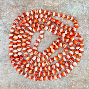 May include: A long strand of red and white agate beads. The beads are round and have a striped pattern. The beads are strung on a clear cord.