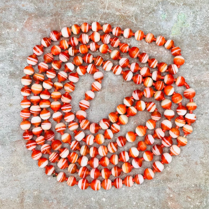 May include: A long strand of red and white agate beads. The beads are round and have a striped pattern. The beads are strung on a clear cord.
