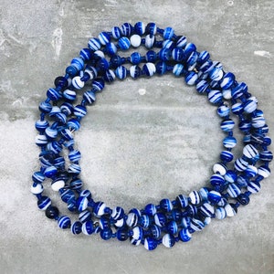 May include: A long necklace made of blue and white striped beads. The beads are round and have a glossy finish.
