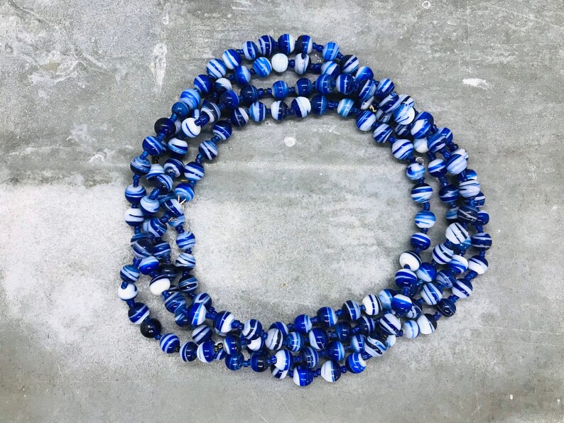 May include: A long necklace made of blue and white striped beads. The beads are round and have a glossy finish.