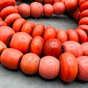 Könnte beinhalten: Eine Korallenkette in leuchtend orange. Die Perlen sind glatt und rund und auf einer durchsichtigen Schnur aufgefädelt.