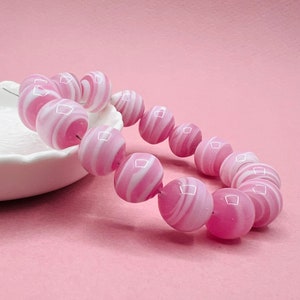 May include: A pink and white striped glass bead bracelet. The beads are round and have a glossy finish.