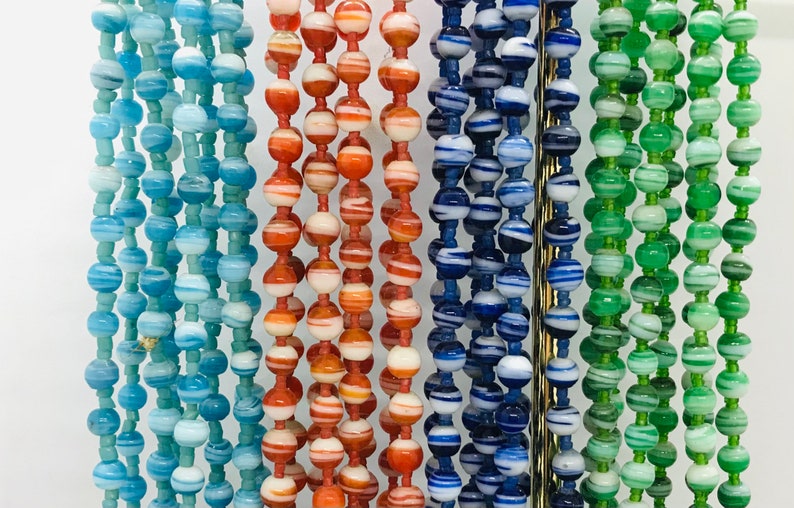 May include: Five strands of colorful glass beads. Each strand features a different color combination of blue, green, white, and orange.