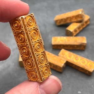 Peut inclure: Un ensemble de six pièces décoratives en métal couleur or avec un motif complexe en spirale. Les pièces sont de forme rectangulaire et ont une finition lisse et polie.