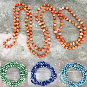 May include: Three strands of colorful beaded necklaces. The first necklace is orange and white, the second is blue and white, and the third is light blue and white.