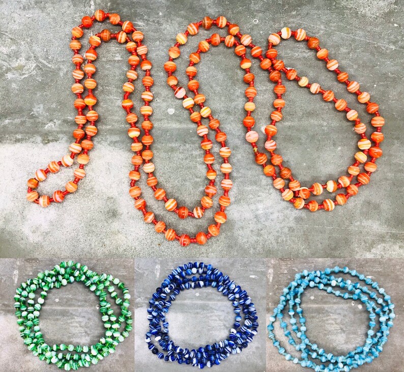 May include: Three strands of colorful beaded necklaces. The first necklace is orange and white, the second is blue and white, and the third is light blue and white.