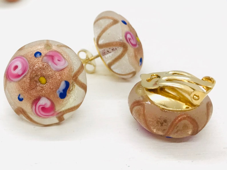 May include: A pair of gold clip-on earrings with round, clear glass stones. The stones are decorated with pink, blue, and gold swirls and dots.