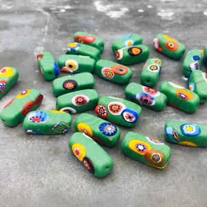 May include: A collection of green glass beads with colorful, multi-colored, and patterned designs. The beads are rectangular in shape and have a glossy finish.