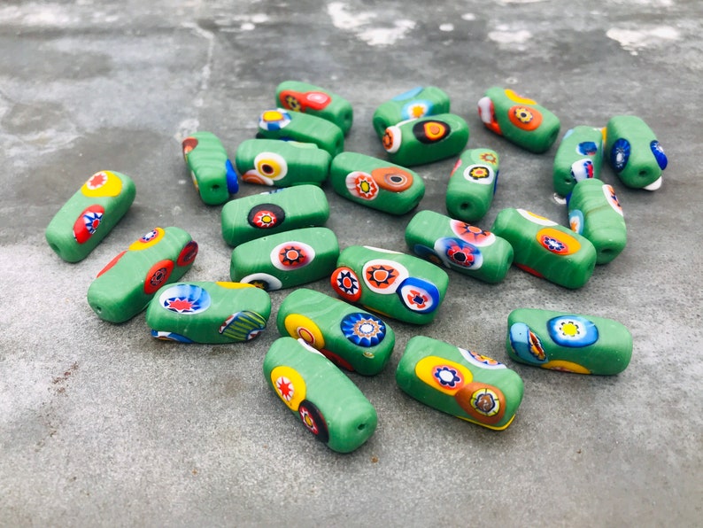May include: A collection of green glass beads with colorful, multi-colored, and patterned designs. The beads are rectangular in shape and have a glossy finish.