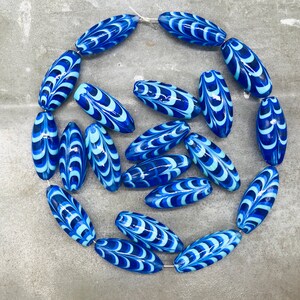 May include: A strand of blue and white glass beads with a swirling pattern. The beads are oval shaped and have a glossy finish.