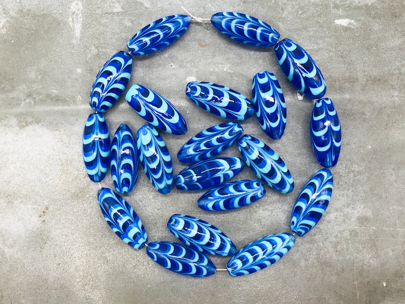 May include: A strand of blue and white glass beads with a swirling pattern. The beads are oval shaped and have a glossy finish.