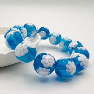 May include: A blue and white glass bracelet with a floral design. The bracelet is made of round beads with white flowers on a blue background.