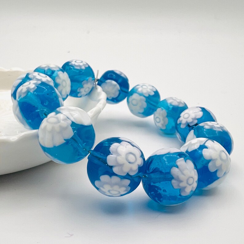 May include: A blue and white glass bracelet with a floral design. The bracelet is made of round beads with white flowers on a blue background.