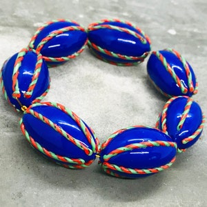Op de afbeelding: Een armband gemaakt van blauwe, groene en oranje ovale kralen. De kralen zijn versierd met een touwachtig patroon.