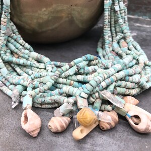 K&ouml;nnte beinhalten: Eine t&uuml;rkisfarbene und wei&szlig;e Perlenkette mit Muschel- und Kristall-Akzenten. Die Kette besteht aus vielen Perlenstr&auml;ngen und hat verschiedene Anh&auml;nger.