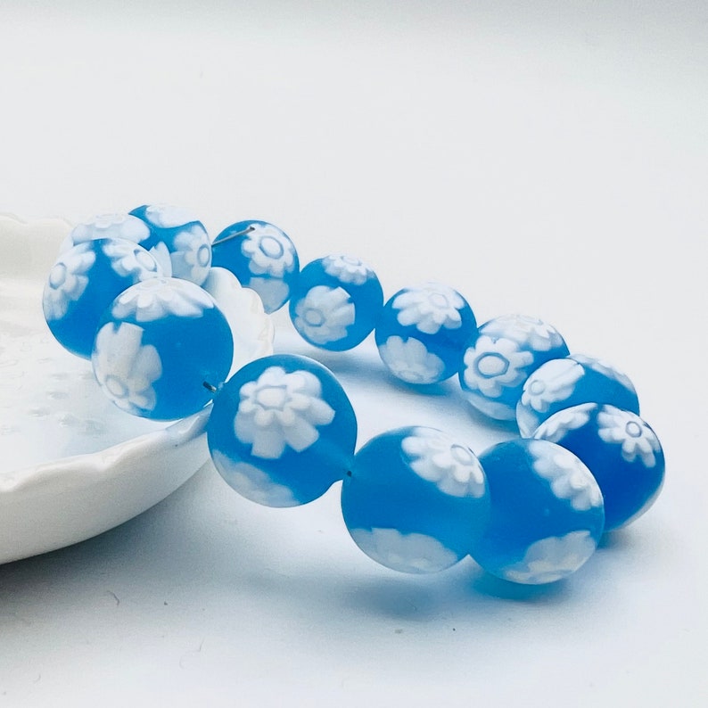 May include: A blue and white beaded bracelet with a floral design. The beads are round and have a frosted finish.