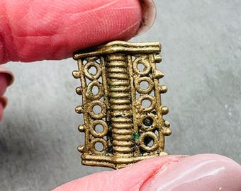 May include: A gold-colored metal pendant with a decorative design of circles and lines. The pendant is about 2 inches long and has a slightly textured surface.