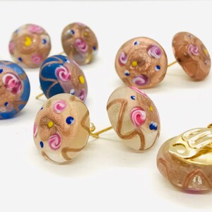 May include: A set of colorful glass earrings with a gold finish. The earrings feature a variety of patterns and colors, including pink, blue, and gold. The earrings are available in both stud and clip-on styles.