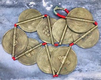 May include: A gold necklace with round, decorative metal discs connected by red beads. Each disc has a different design, including a spider, a fish, and a geometric pattern.