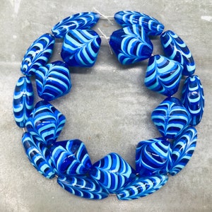 May include: A string of blue and white glass beads with a swirling pattern. The beads are arranged in a circle.
