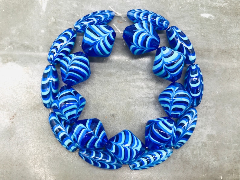 May include: A string of blue and white glass beads with a swirling pattern. The beads are arranged in a circle.