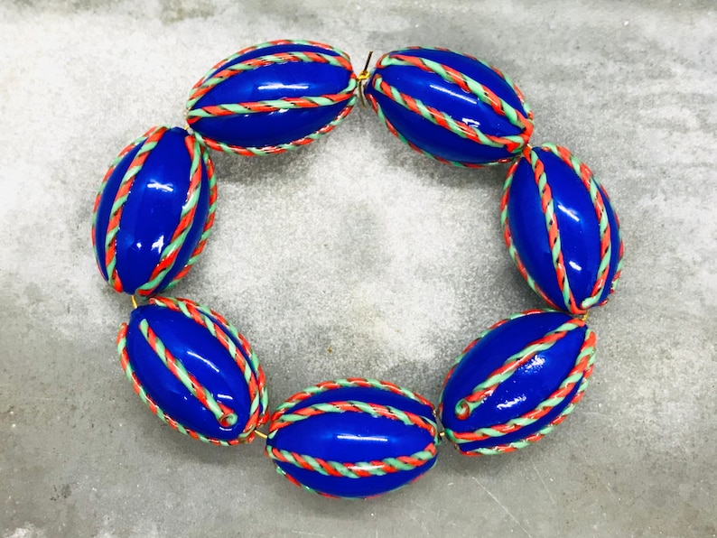 Op de afbeelding: Een blauwe en witte ovale kralenketting met een gouden sluiting. De kralen zijn versierd met rode en groene strepen.