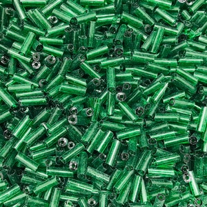 Op de afbeelding: Een close-up van een grote hoeveelheid kleine, groene glazen kralen. De kralen zijn cilindrisch van vorm en hebben een licht iriserende afwerking.