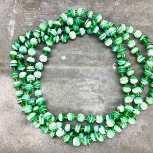 May include: A long strand of green and white striped beads. The beads are made of glass and have a swirling pattern.