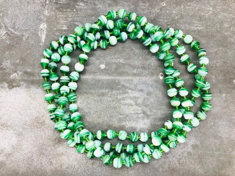 May include: A long strand of green and white striped beads. The beads are made of glass and have a swirling pattern.