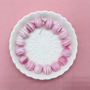 May include: A strand of pink and white striped glass beads on a white plate with a decorative pattern.