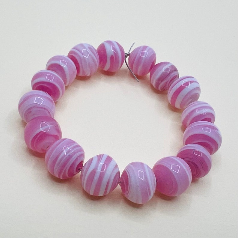 May include: A pink and white glass bead bracelet with a swirl pattern. The beads are round and have a glossy finish.