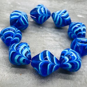 May include: A strand of blue and white glass beads with a swirling pattern. The beads are faceted and have a diamond shape.