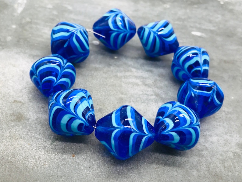 May include: A strand of blue and white glass beads with a swirling pattern. The beads are faceted and have a diamond shape.