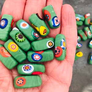 May include: A collection of green glass beads with colorful, patterned designs. The beads are rectangular and have a variety of colors, including red, yellow, blue, and white.