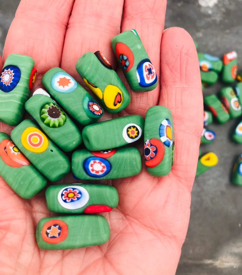 May include: A collection of green glass beads with colorful, patterned designs. The beads are rectangular and have a variety of colors, including red, yellow, blue, and white.