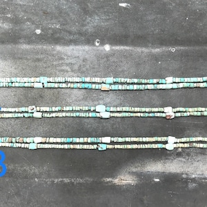 K&ouml;nnte beinhalten: Drei Str&auml;nge von Halsketten aus t&uuml;rkisfarbenen und wei&szlig;en Perlen mit unterschiedlichen Endst&uuml;cken. Die obere Halskette hat ein kleines, braunes, pfeilf&ouml;rmiges Endst&uuml;ck. Die mittlere Halskette hat ein wei&szlig;es, knochenartiges Endst&uuml;ck. Die untere Halskette hat ein wei&szlig;es, rechteckiges Endst&uuml;ck.