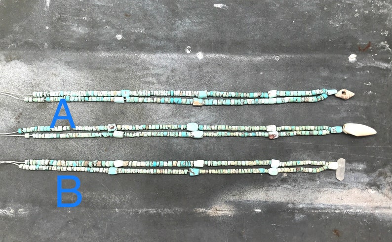 K&ouml;nnte beinhalten: Drei Str&auml;nge von Halsketten aus t&uuml;rkisfarbenen und wei&szlig;en Perlen mit unterschiedlichen Endst&uuml;cken. Die obere Halskette hat ein kleines, braunes, pfeilf&ouml;rmiges Endst&uuml;ck. Die mittlere Halskette hat ein wei&szlig;es, knochenartiges Endst&uuml;ck. Die untere Halskette hat ein wei&szlig;es, rechteckiges Endst&uuml;ck.