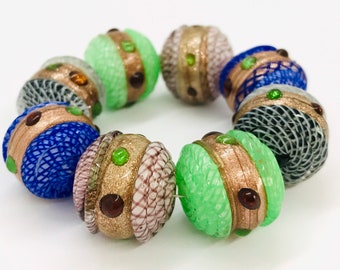 May include: A set of eight colorful glass beads with intricate patterns and gold accents. The beads are round and have a variety of colors, including green, blue, and brown.