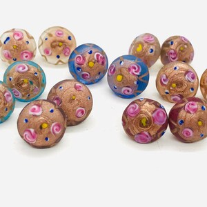 May include: Assortment of colorful glass beads with intricate floral patterns and gold accents. The beads are round and have a glossy finish.